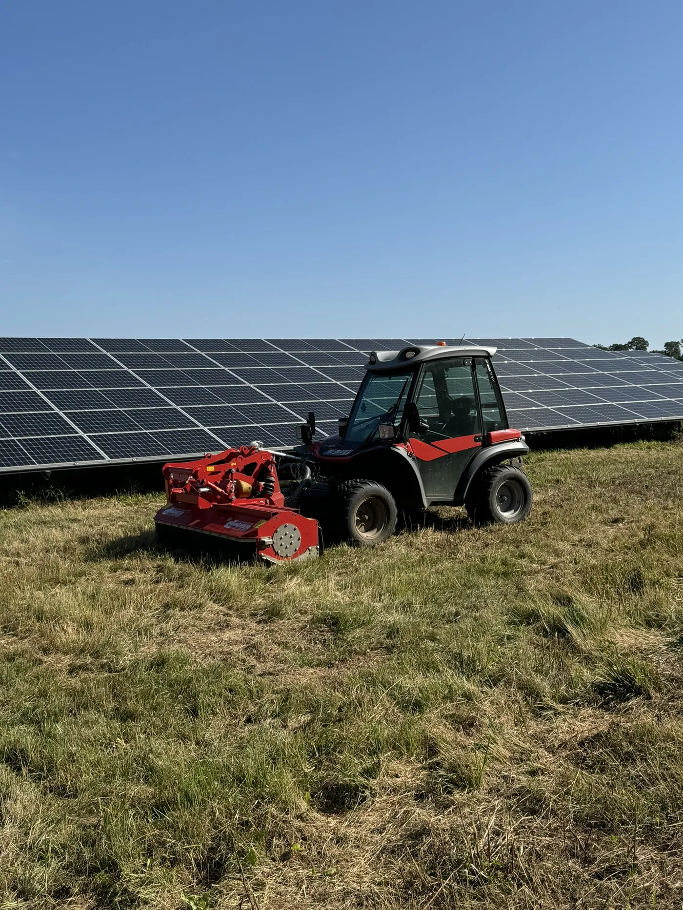 Solarparkpflege – Kompakttraktor mit Mähwerk vor Solarpanels